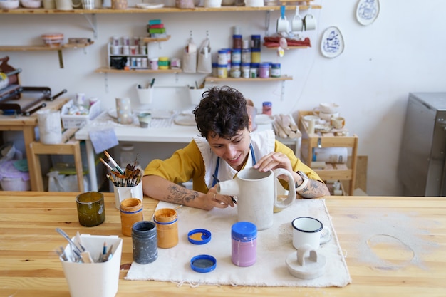 Junge glückliche Künstlerin konzentrierte sich auf das Malen und Dekorieren von Keramik in einem Workshop für Kunstkurse