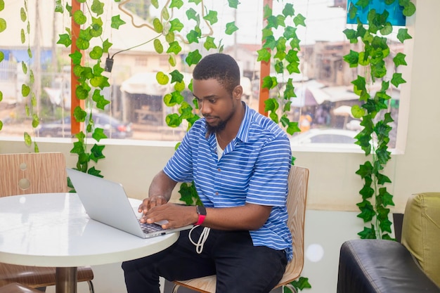 Junge, glückliche, lächelnde afroamerikanische Mann sitzt und benutzt einen Laptop