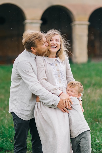 Junge glückliche liebende Familie, die im Regen umarmt. Authentische Familie in Leinenkostümen mit einem Kind in Regentropfen