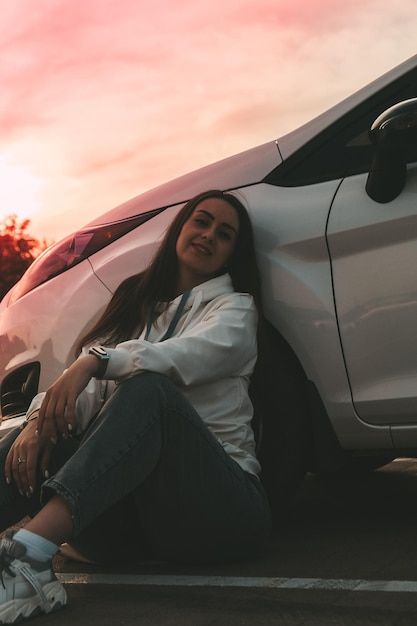 Foto junge, glückliche, millenniale, brünette frau sitzt neben dem auto, junge, attraktive frau im auto.