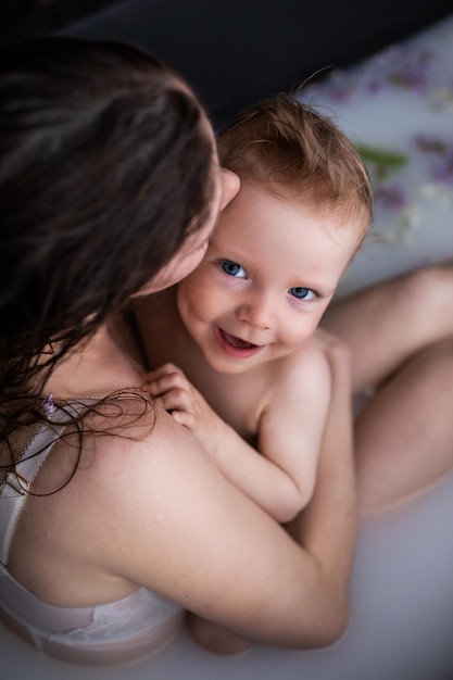 Junge glückliche Mutter mit kleinem Sohn im Blumenmilchbad Mutter und Kind zärtlich umarmend im Bad