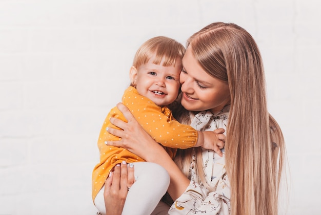 Junge glückliche Mutter umarmt ihre kleine lachende Tochter. Mama und ihr Kind haben zusammen Spaß