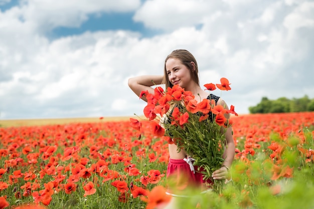 Junge glückliche ukrainische Frau, die Blumenstrauß von Mohnblumenblumen geht und sonnigen Tag im Feld genießt