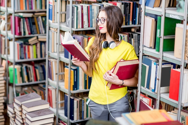 Junge glückliche und enthusiastische Studentin, die Bücher in der alten Bibliothek liest