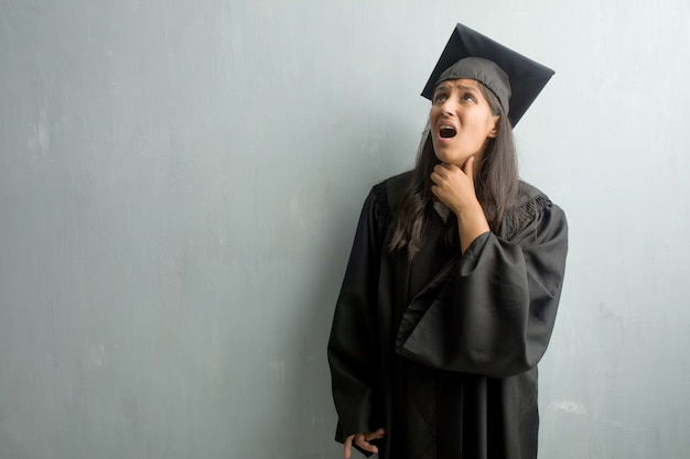 Junge graduierte indische Frau gegen eine Wand besorgt und überwältigt, besorgter Gefühlsdruck, Konzept der Angst