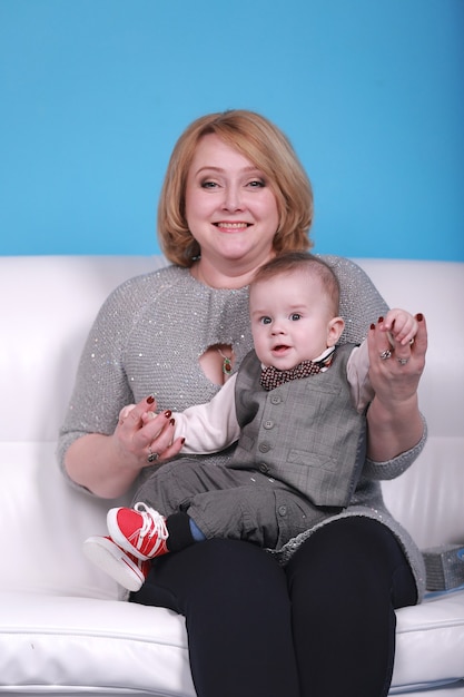 Junge Großmutter mit ihrem kleinen Enkel auf einem weißen Sofa. Blaue Wand mit einem weißen Mond und Sternen an einer Wand.