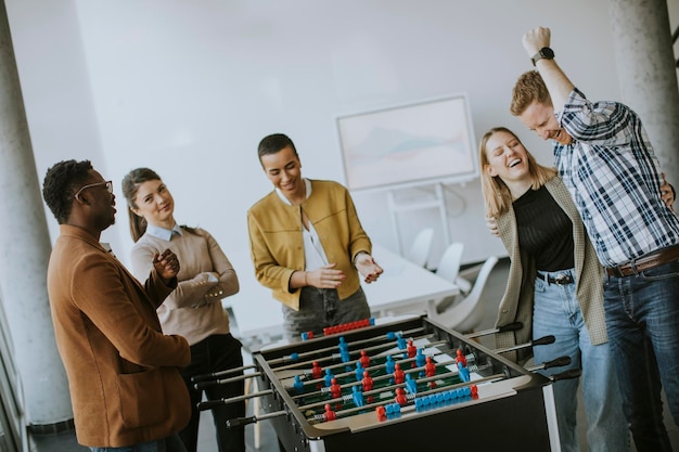 Junge, gutaussehende, lässige, multiethnische Geschäftsleute, die Tischfußball spielen und sich im Büro entspannen