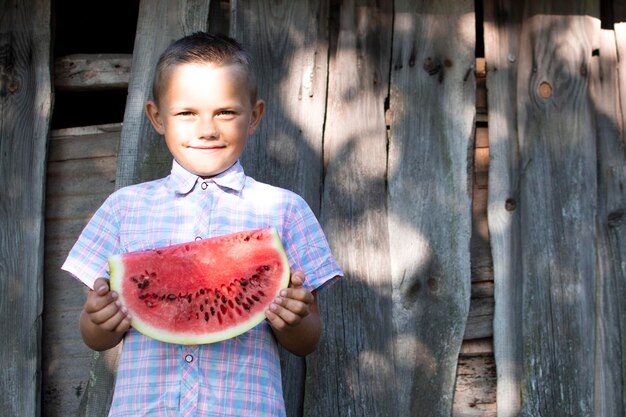 Junge hält ein großes Stück Wassermelone gegen eine hölzerne ländliche Wand