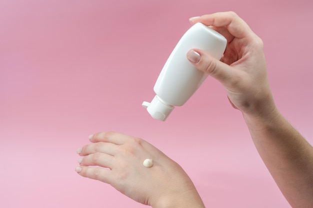 Junge Hände quetschen Creme aus Tube auf rosa Hintergrund Für Schönheits- oder Medizinprodukte