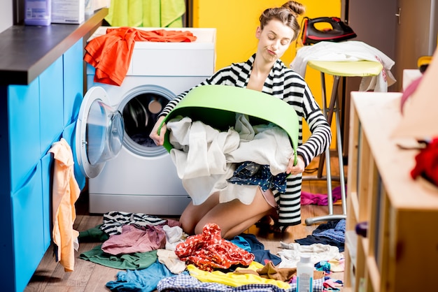Junge Hausfrau sitzt mit Kleiderkorb in der Nähe der Waschmaschine zu Hause