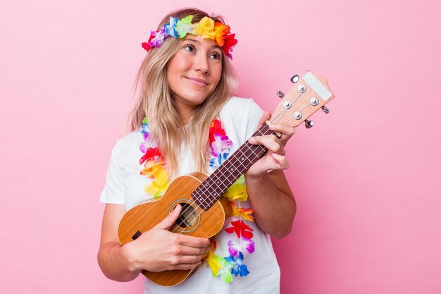 Junge hawaiianische Frau, die eine Ukulele spielt, die auf rosa Hintergrund lokalisiert wird