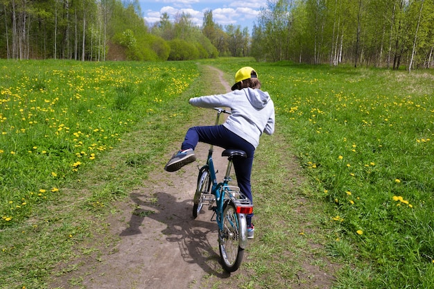 Junge hebt sein Bein und setzt sich auf die Rückansicht des Fahrrads auf dem Hintergrund der Sommernatur