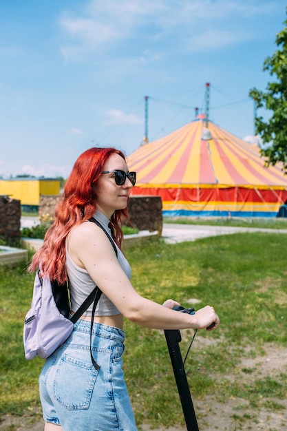 Junge helle Frau lächelt und fährt Elektroroller im Sommer in der Stadt