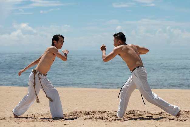 Junge hemdlose Männer üben gemeinsam Capoeira am Strand