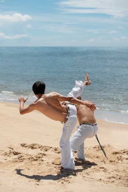 Junge hemdlose Männer üben gemeinsam Capoeira am Strand