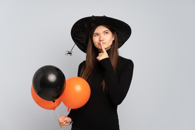 Junge Hexe, die schwarze und orange Luftballons hält