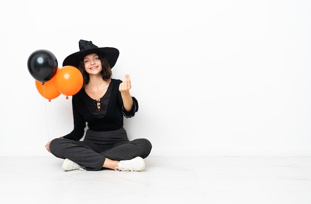 Junge Hexe, die schwarze und orange Luftballons hält