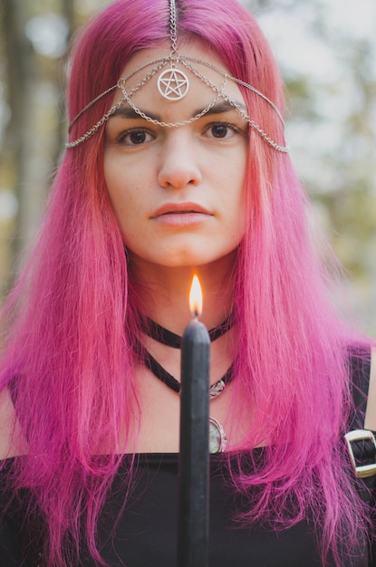 Junge hexe mit dem rosa haar, das ein magisches ritual mit einer schwarzen dunklen kerze, verblaßte farben, vorgewählter fokus durchführt