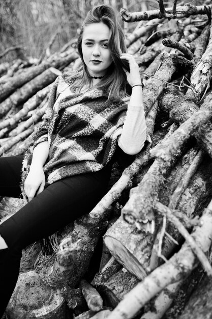 Junge Hippie-Mädchenabnutzung auf Decke gegen hölzerne Stümpfe auf Holz. Schwarzweiss-Foto.