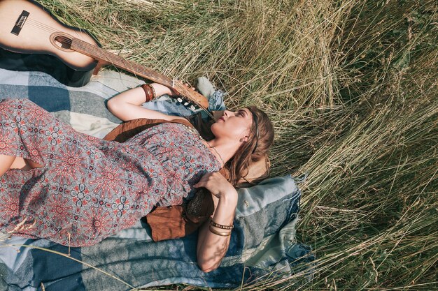 Junge Hippiefrau mit der Gitarre, die auf Gras liegt