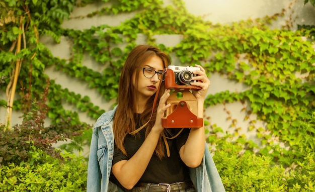 Junge Hipster-Frau in Jeansjacke und Brille genießt Film-Retro-Kamera im Freien