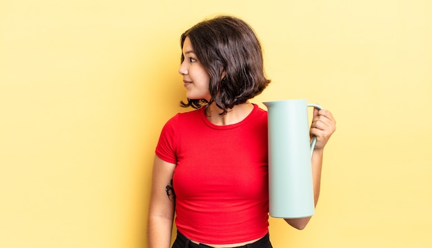 Junge hispanische Frau auf Profilansicht denken, sich vorstellen oder träumen. Thermos-Konzept