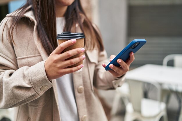 Junge hispanische Frau benutzt Smartphone und trinkt Kaffee auf der Straße