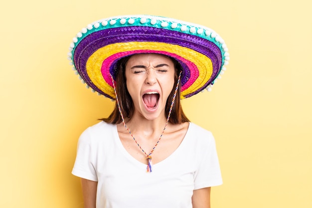 Junge hispanische Frau, die aggressiv schreit und sehr wütend aussieht. mexikanisches Hutkonzept