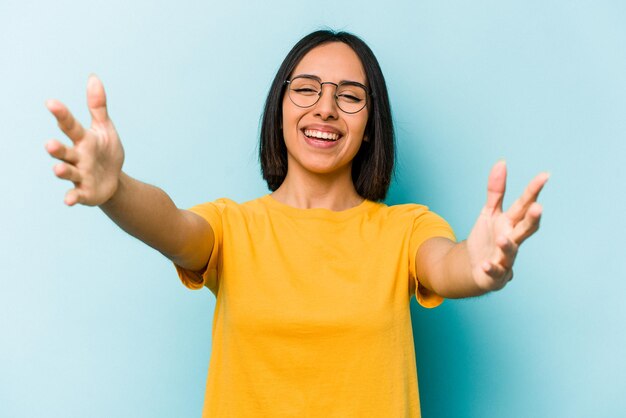 Junge hispanische frau, die auf blauem hintergrund isoliert ist, fühlt sich zuversichtlich, die kamera zu umarmen