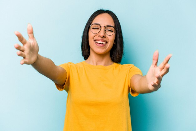 Junge hispanische Frau, die auf blauem Hintergrund isoliert ist, fühlt sich zuversichtlich, die Kamera zu umarmen