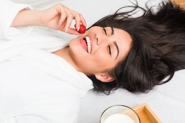 Junge hispanische Frau, die auf dem Bett frühstückt