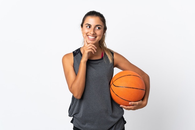 Junge hispanische Frau, die Basketball über isolierte weiße Wand spielt, die eine Idee beim Aufschauen denkt