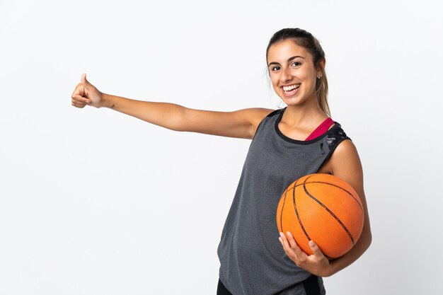 Junge hispanische Frau, die Basketball über isoliertem Weiß spielt, das eine Daumen hoch Geste gibt