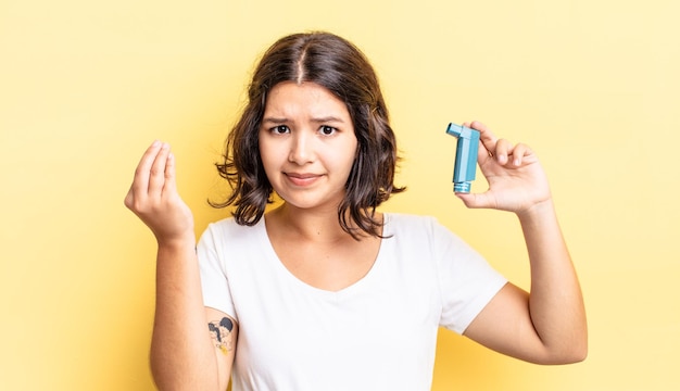 Junge hispanische Frau, die Capice oder Geldgeste macht und Ihnen sagt, dass Sie bezahlen sollen. Asthma-Konzept