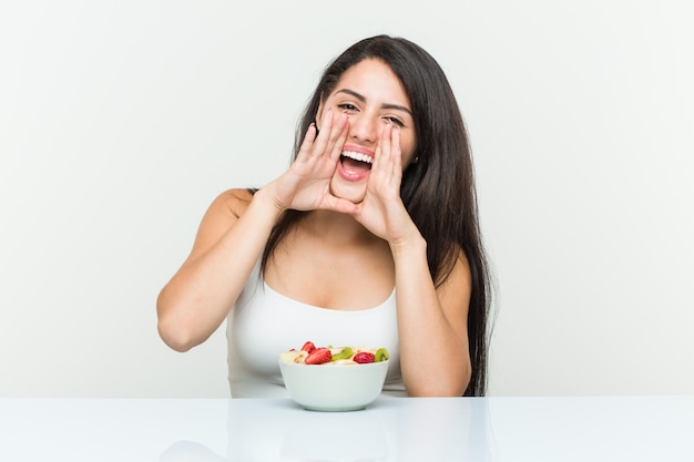 Junge hispanische Frau, die ein Obstschalenschreien aufgeregt nach vorne isst.