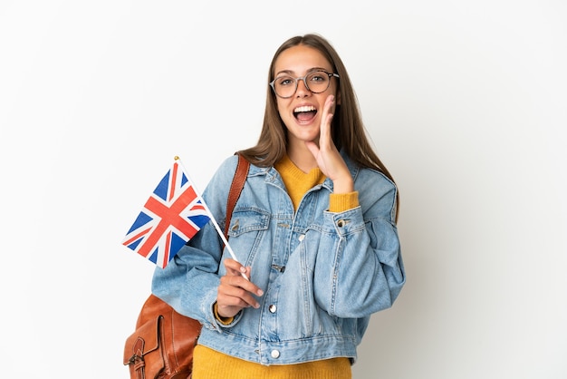 Junge hispanische Frau, die eine britische Flagge über isoliertem weißem Hintergrund hält, der mit dem Mund weit offen schreit