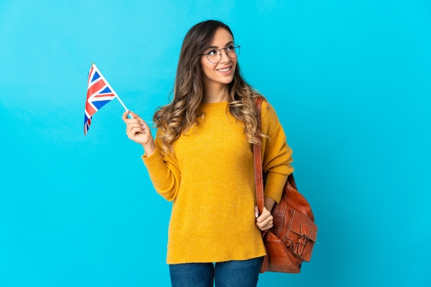 Junge hispanische Frau, die eine Flagge des Vereinigten Königreichs auf Blau hält und eine Idee beim Aufschauen denkt