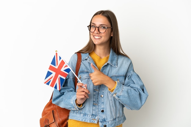 Junge hispanische Frau, die eine Flagge des Vereinigten Königreichs über isoliertem weißem Hintergrund hält und eine Geste mit dem Daumen nach oben gibt