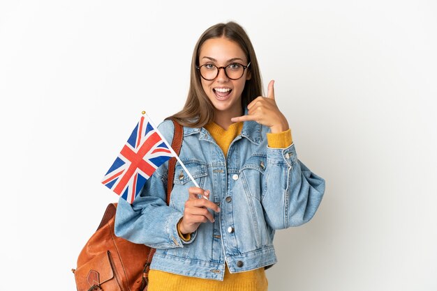 Junge hispanische Frau, die eine Flagge des Vereinigten Königreichs über lokalisiertem weißem Hintergrund hält, der Telefongeste macht. Ruf mich zurück Zeichen