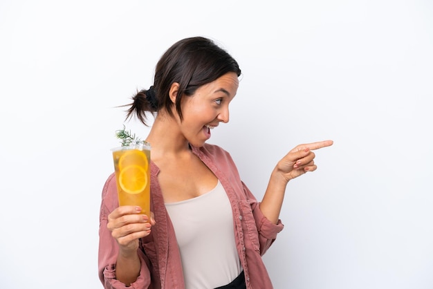 Junge hispanische Frau, die einen Cocktail isoliert auf weißem Hintergrund hält, mit dem Finger zur Seite zeigt und ein Produkt präsentiert