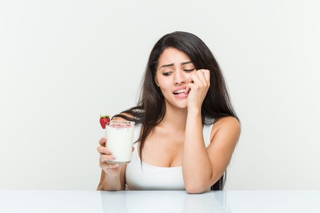 Junge hispanische Frau, die einen Smoothie hält junge hispanische Frau, die einen Avocado-Toast hält, der Fingernägel beißt, nervös und sehr ängstlich