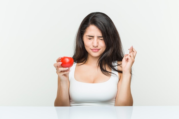 Junge hispanische Frau, die Finger einer Tomatenüberfahrt für das Haben des Glücks hält