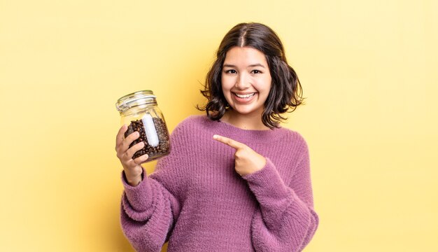 Junge hispanische Frau, die fröhlich lächelt, sich glücklich fühlt und auf die Seite zeigt. Kaffeebohnen-Konzept