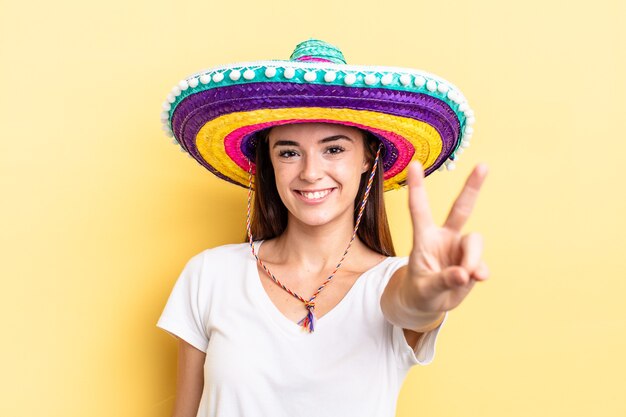 Junge hispanische Frau, die glücklich lächelt und schaut und Sieg oder Frieden gestikuliert. mexikanisches Hutkonzept