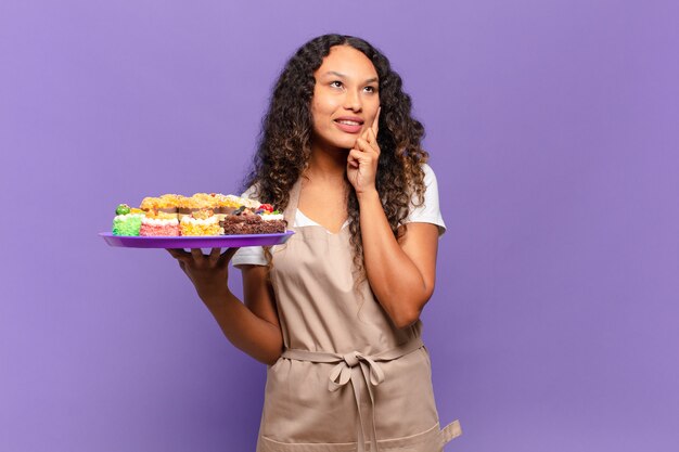 Junge hispanische Frau, die glücklich lächelt und träumt oder zweifelt und zur Seite schaut. Kuchenkonzept kochen