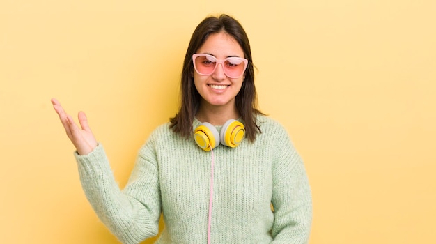 Junge hispanische Frau, die glücklich überrascht ist, ein Lösungs- oder Ideenkopfhörer- und -sonnenbrillenkonzept zu realisieren