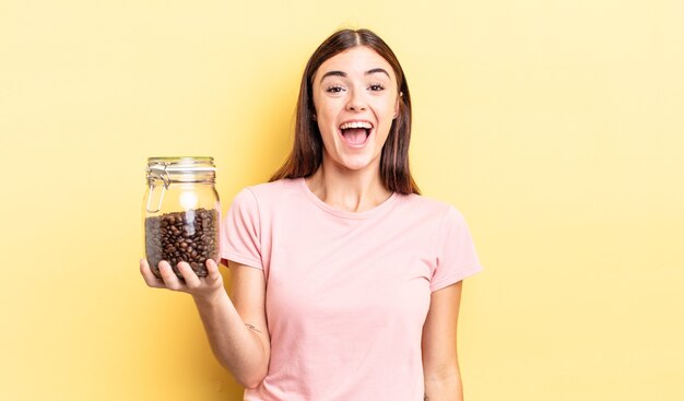 Junge hispanische Frau, die glücklich und angenehm überrascht aussieht. Kaffeebohnen-Konzept