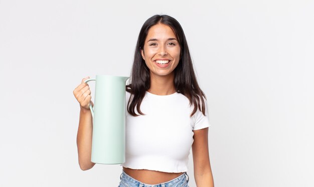 Junge hispanische Frau, die glücklich und angenehm überrascht aussieht und eine Kaffeethermos hält