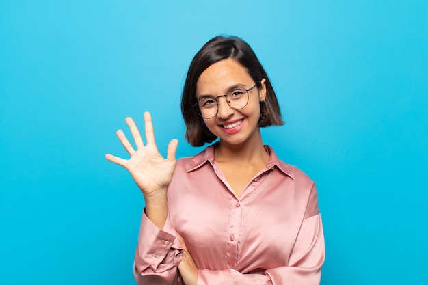 Junge hispanische Frau, die lächelt und freundlich aussieht, Nummer fünf oder fünften mit der Hand nach vorne zeigend, Countdown