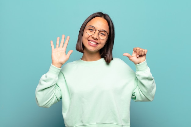 Junge hispanische Frau, die lächelt und freundlich aussieht, Nummer sechs oder Sechste mit der Hand nach vorne zeigend, Countdown